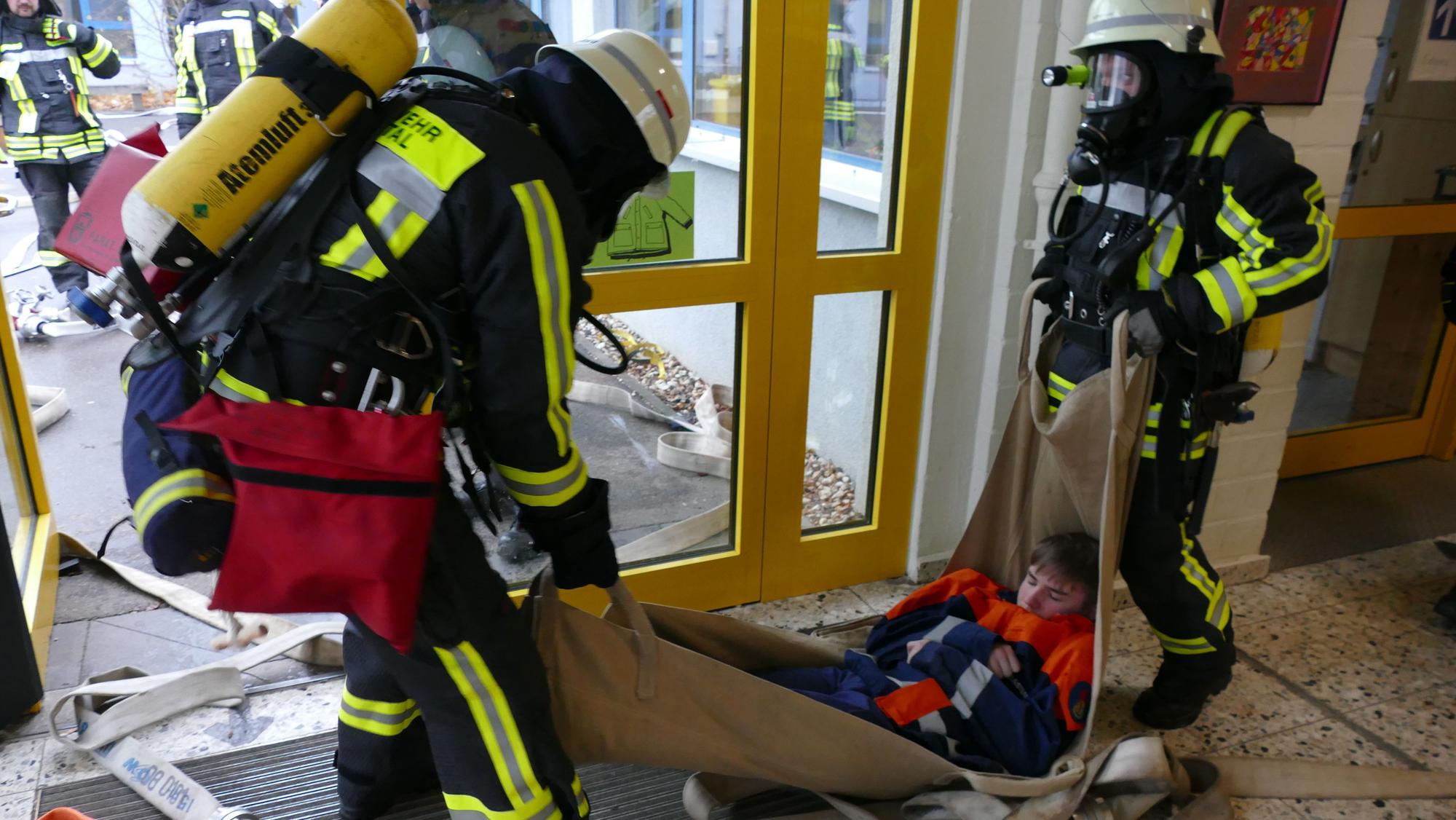 Feuerwehrleute tragen bei der Übung eine bewusstlose Person nach draußen.