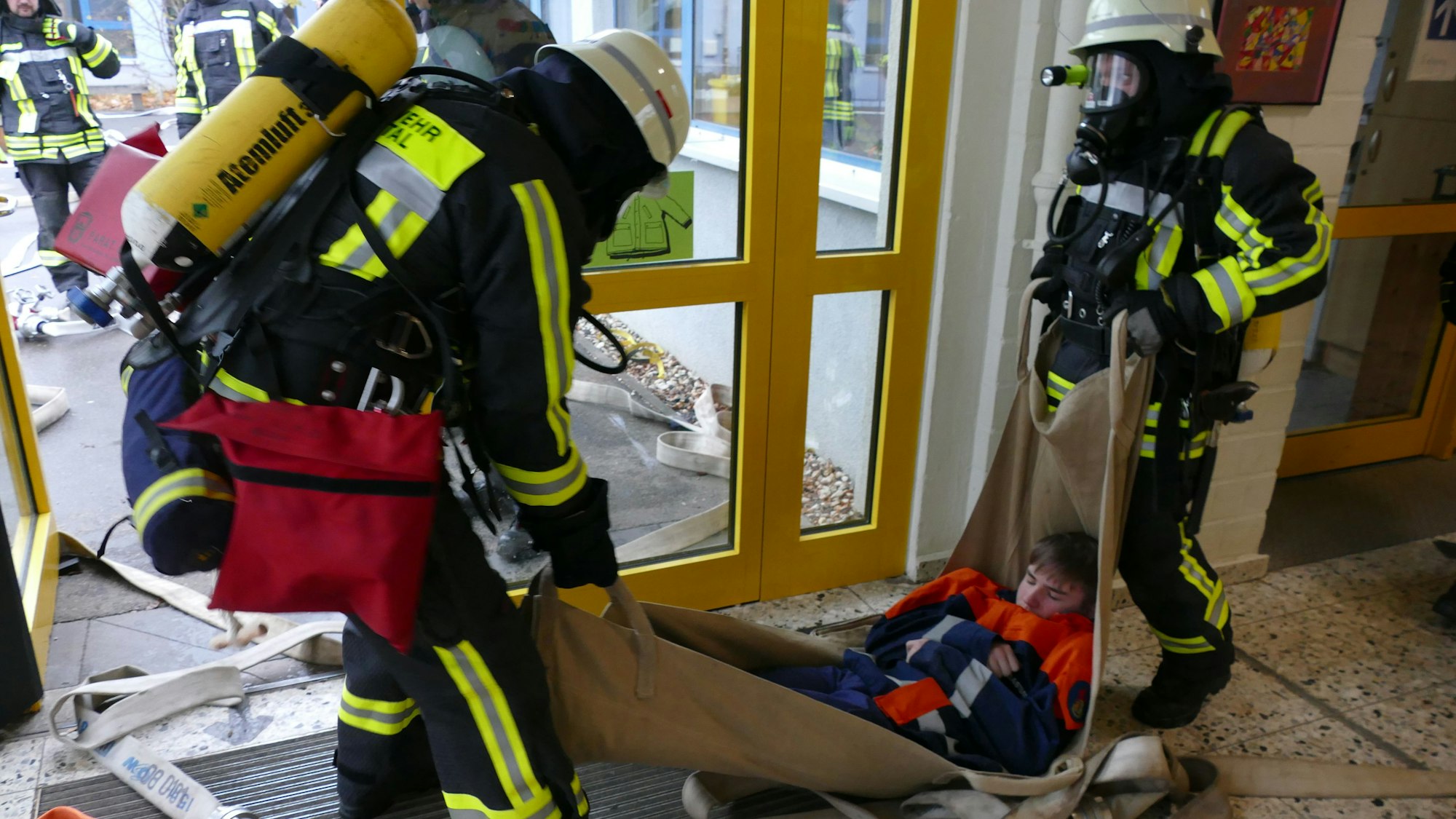 Feuerwehrleute tragen bei der Übung eine bewusstlose Person nach draußen.