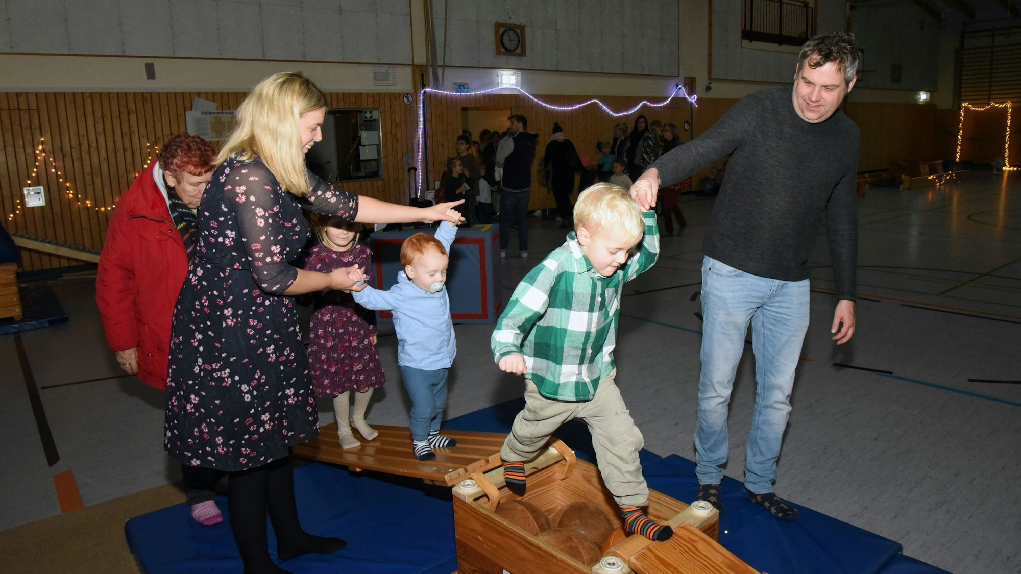 Zwei Kinder balancieren mit Hilfe ihrer Eltern über Turngeräte.