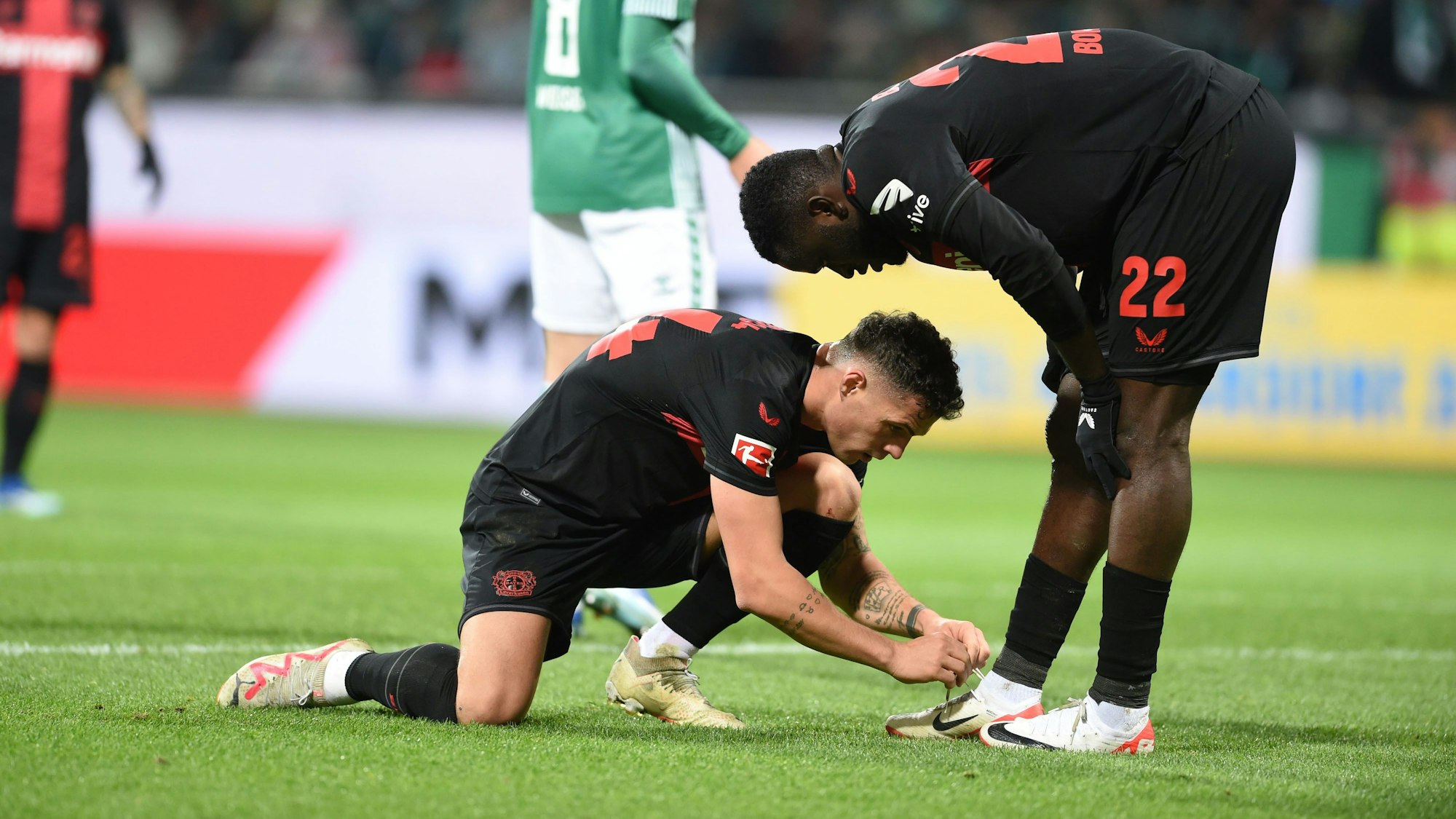 Leverkusens Granit Xhaka schnürt Victor Boniface die Schuhe. Das Spiel endete 0:3. Foto: Carmen Jaspersen/dpa -