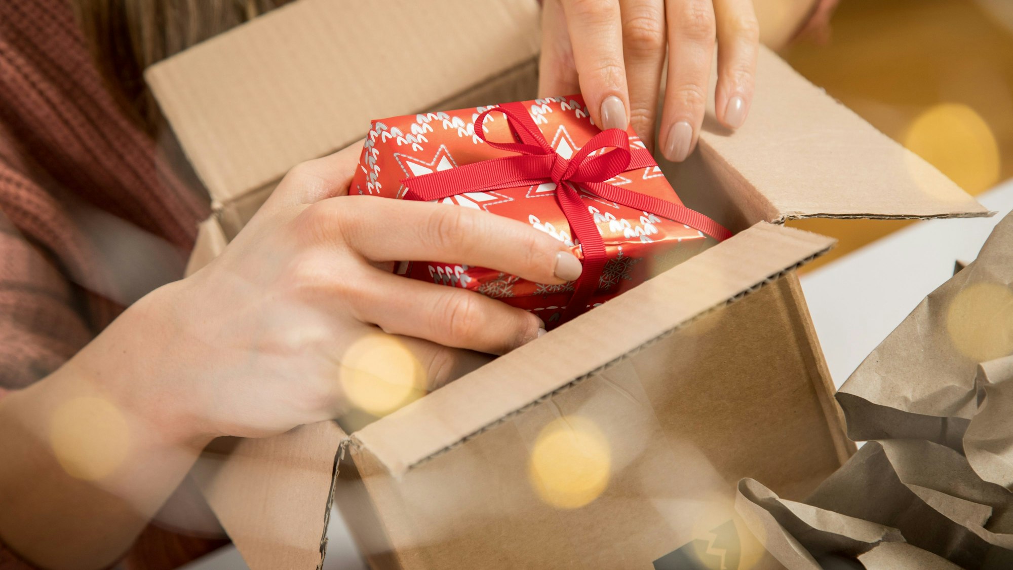 Eine Person legt ein kleines Weihnachtsgeschenk in einen Karton.