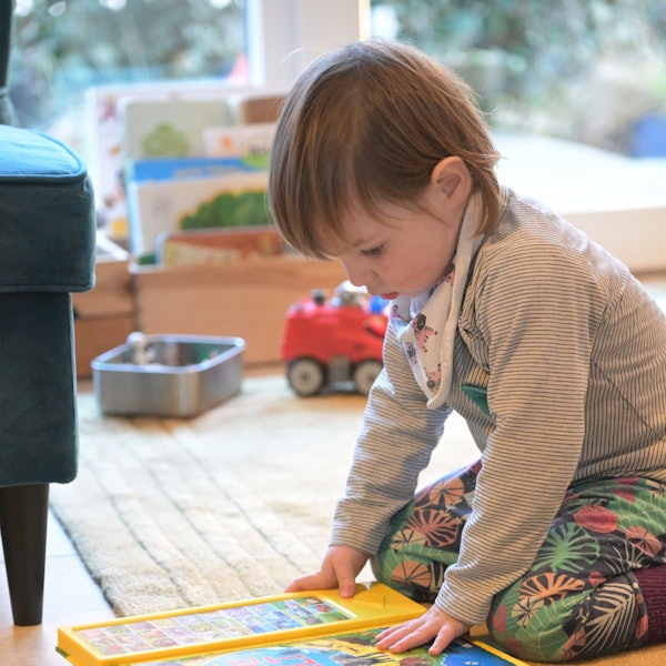 Das Mädchen sitzt auf dem Boden im Wohnzimmer und sieht sich ein Bilderbuch an.