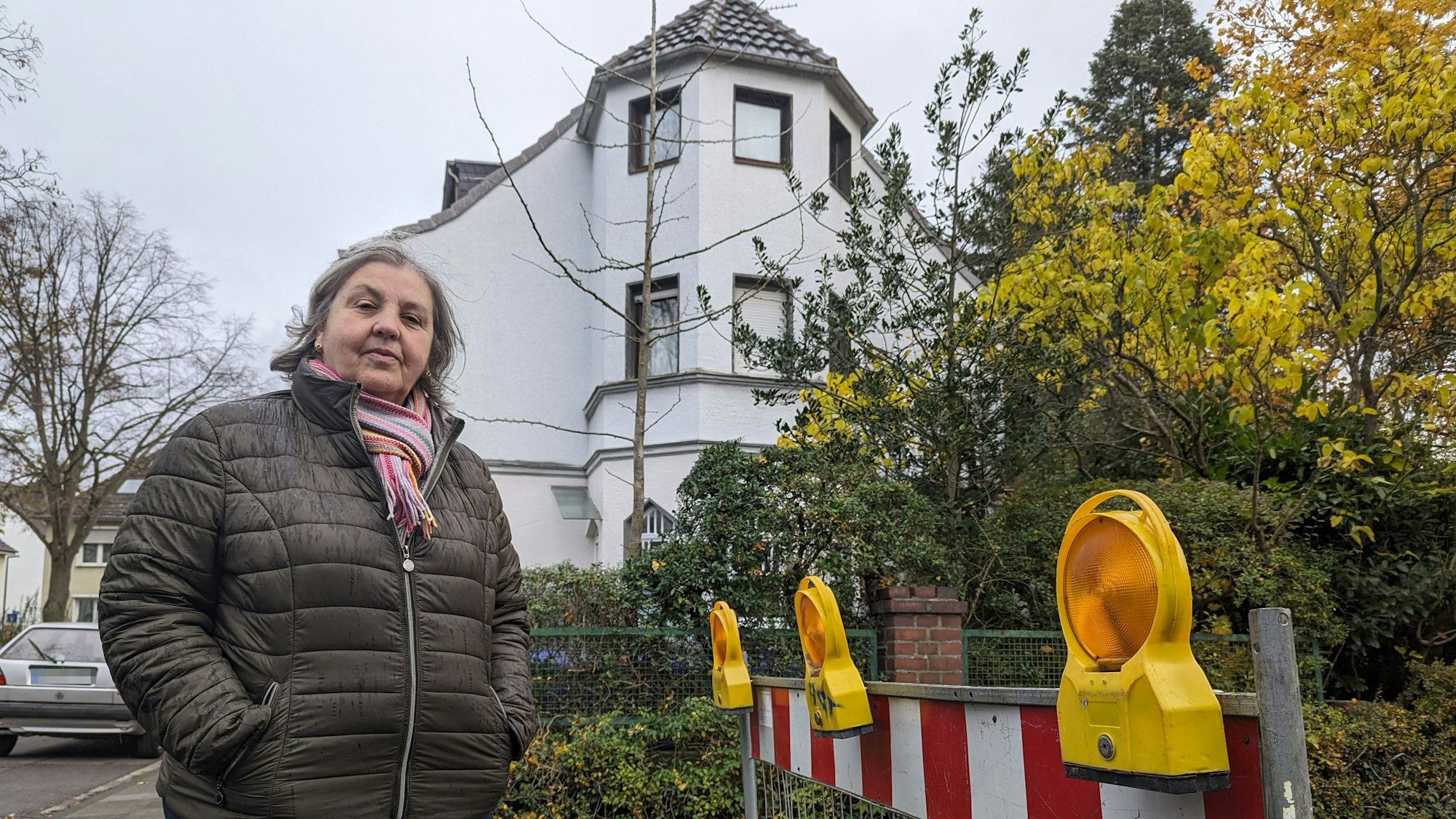 Eine Frau steht neben einer Baustellenabsperrung, im Hintergrund ist ihr Wohnhaus zu sehen.