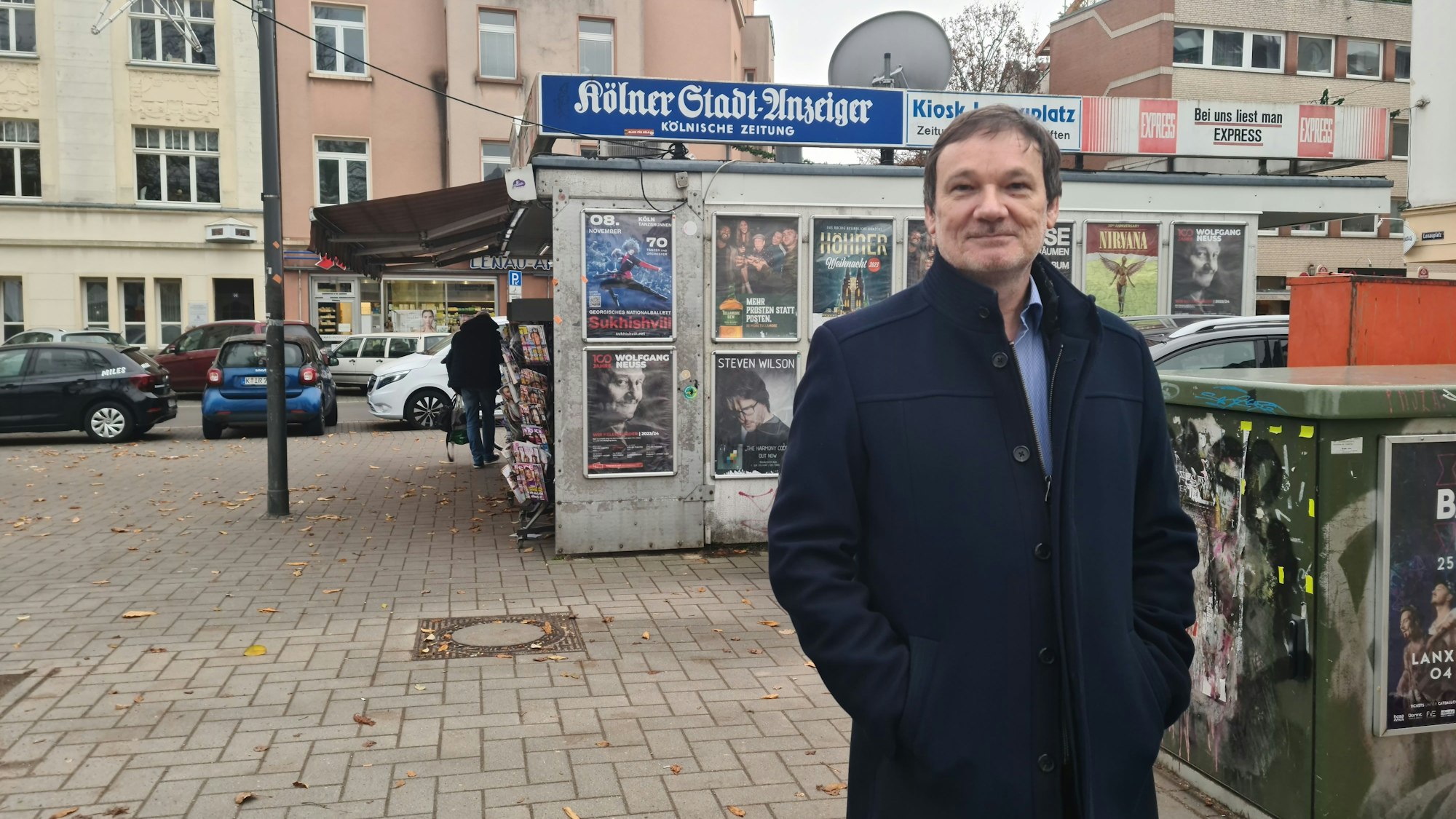 Ein Mann mit den Händen in den Manteltaschen steht hinter einer Tischtennisplatte.