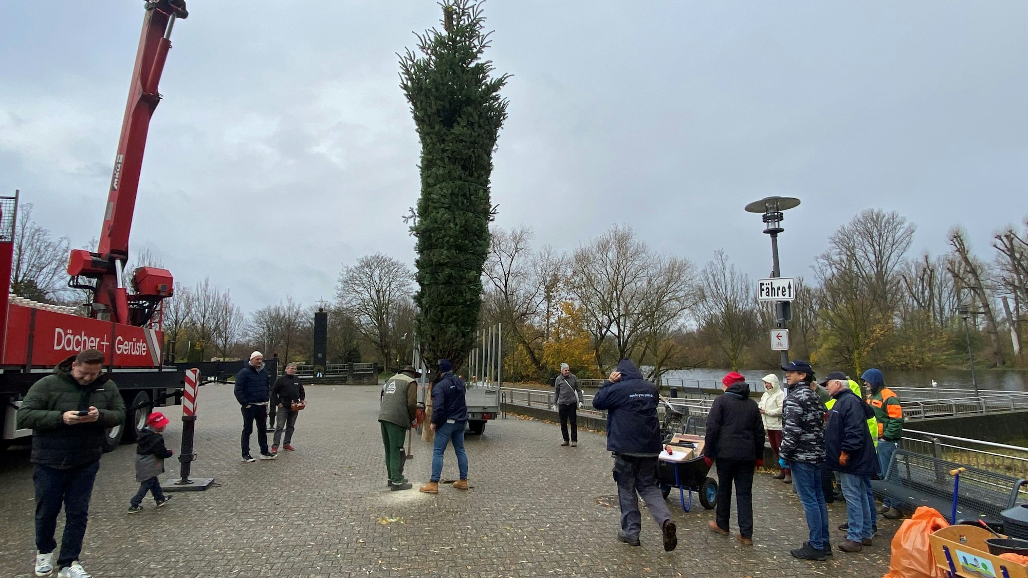 Ein Kran hebt einen Weihnachtsbaum auf den Zündofer Marktplatz. Helfer schauen zu.