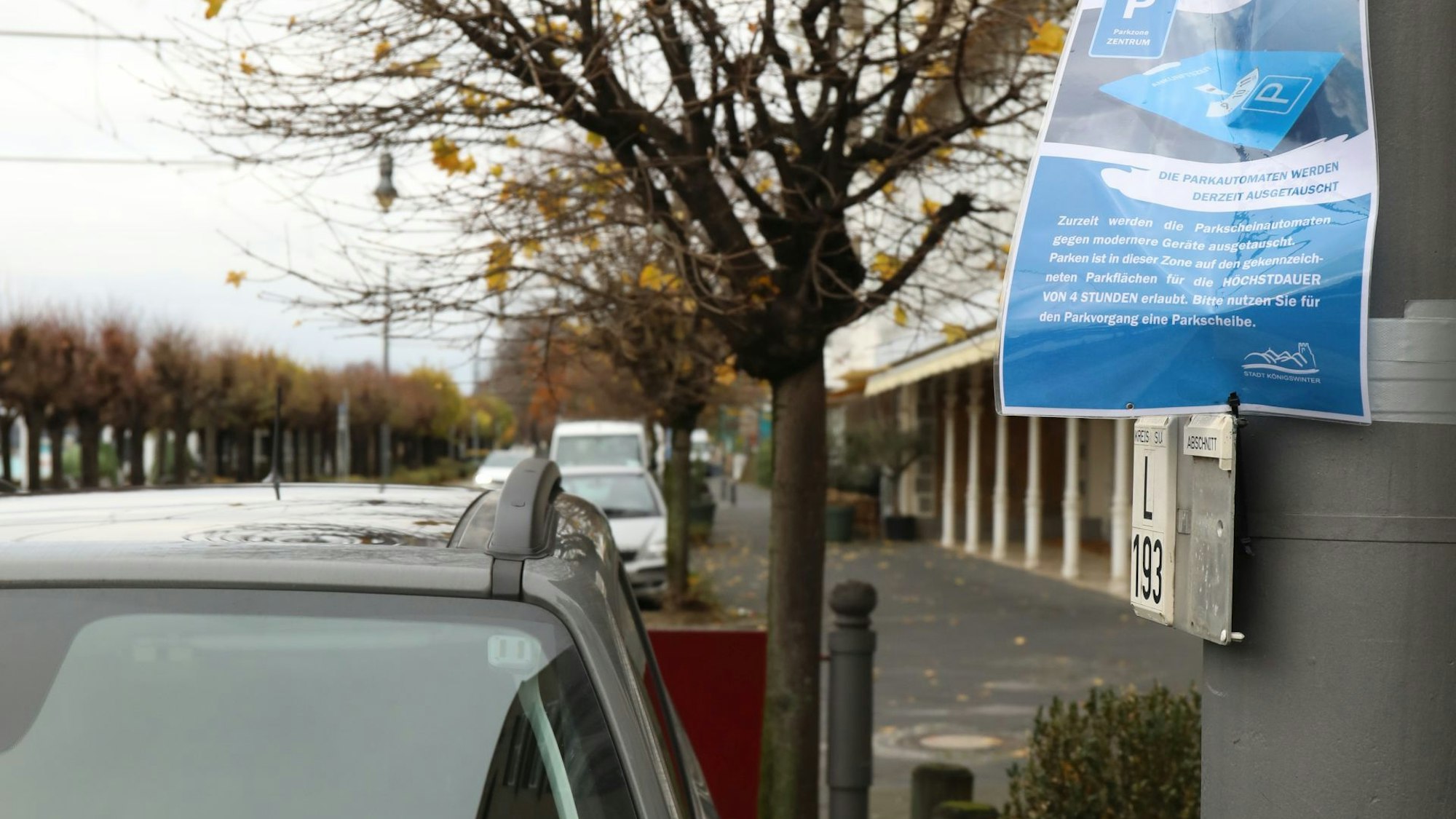 An einem Laternenpfahl neben parkenden Autos hängt ein laminiertes blaues Schild, auf dem die Stadt Autofahrer bittet, die Parkscheibe hinter die Windschutzscheibe zu legen.