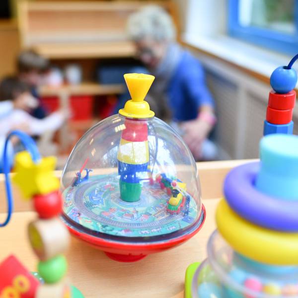 Eine Erzieherin spielt in einer Kita mit Kindern. Im Vordergrund steht Spielzeug.