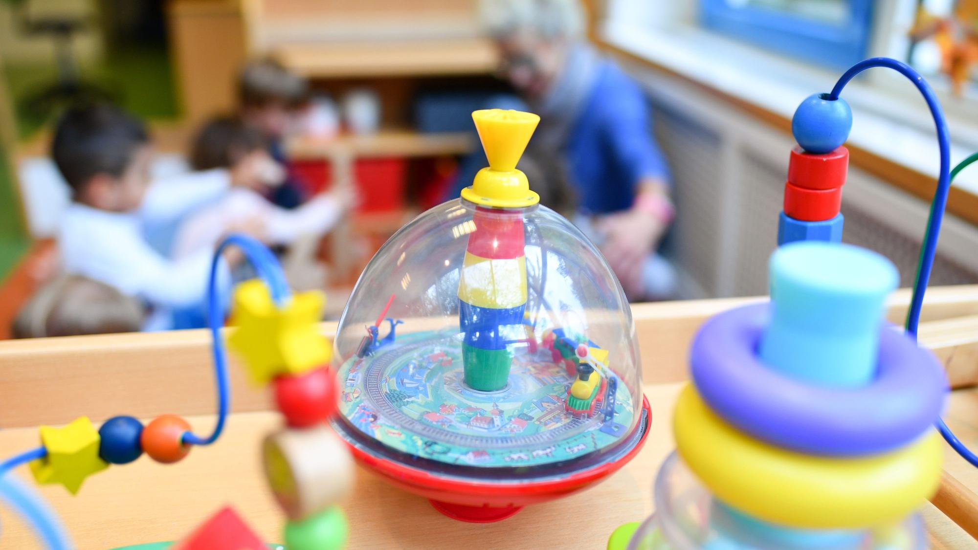 Eine Erzieherin spielt in einer Kita mit Kindern. Im Vordergrund steht Spielzeug.