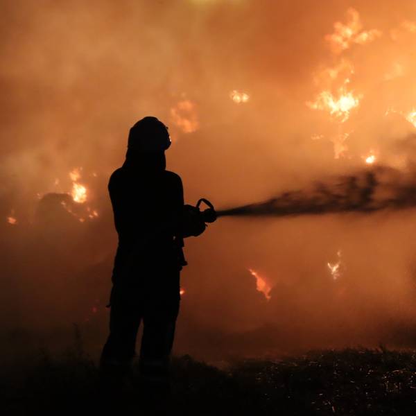 Das Bild zeigt einen Feuerwehrmann, der vor einer Feuerwand steht.