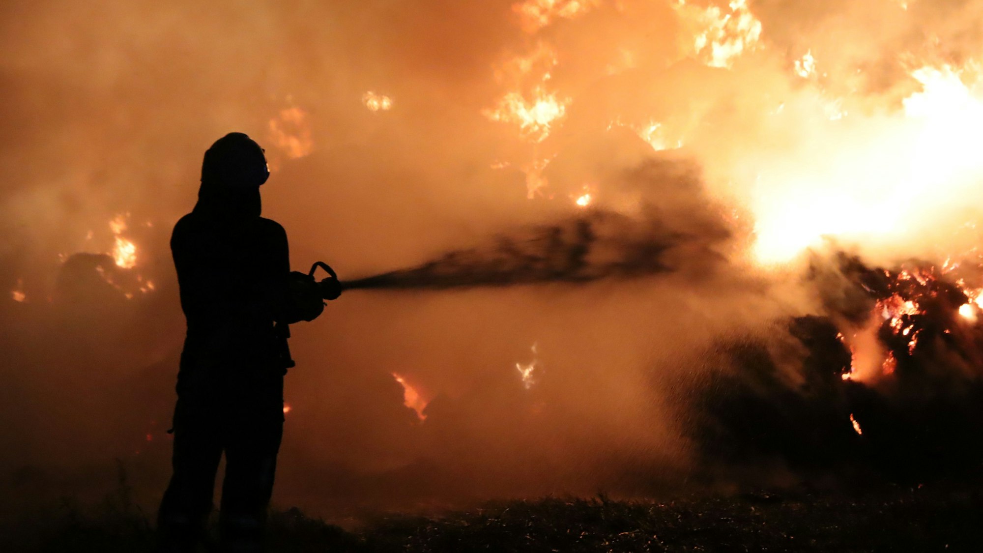 Das Bild zeigt einen Feuerwehrmann, der vor einer Feuerwand steht.