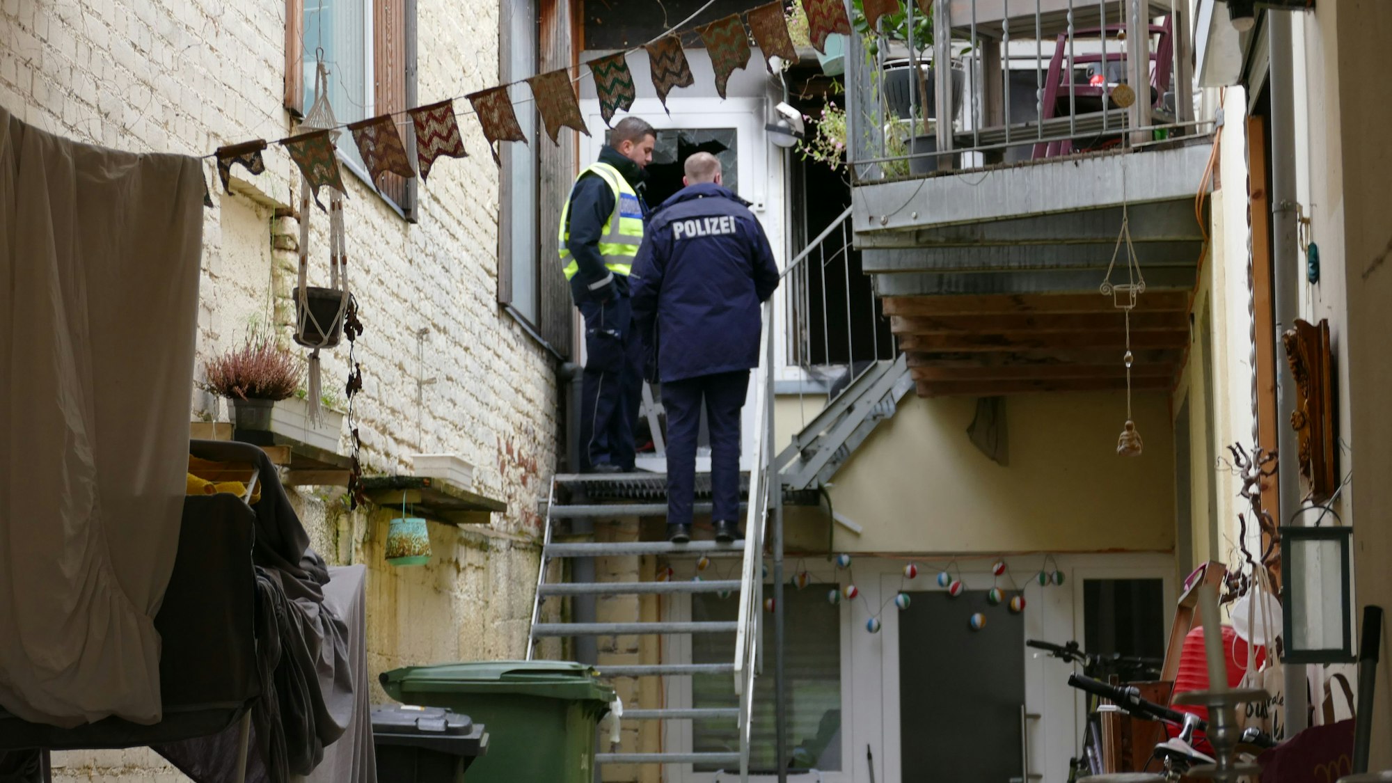 Ein Polizist und ein städtischer Bediensteter stehen vor einer Wohnung in einem Hinterhof.