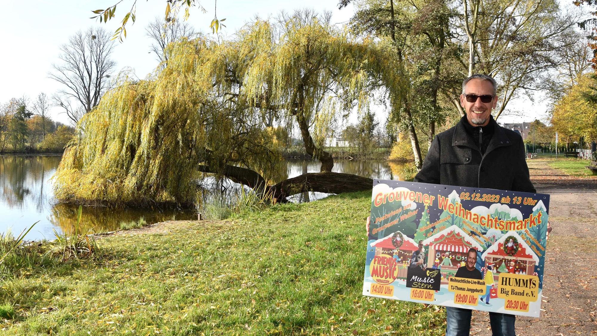 Zu sehen ist Ralf Gohrbandt, der vor dem Grouvener Weiher steht und ein Weihnachtsmarkt-Plakat in den Händen hält.