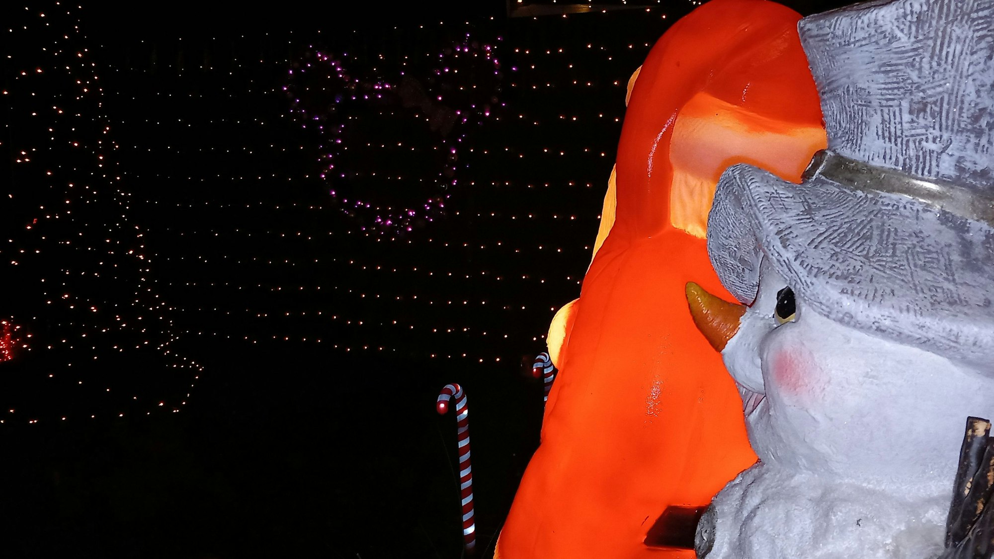 Weihnachtsmann und Schneemann haben neben der Haustür einen Blick auf eine Hecke mit leuchtender Mickey Mouse und einen Stabtannenbaum sowie Zuckerstangen.