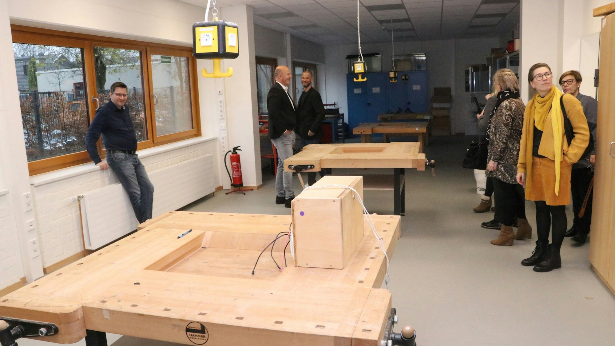 Gäste der Einweihungsfeier schauen sich einen Raum mit mehreren Werkbänken aus Holz an.