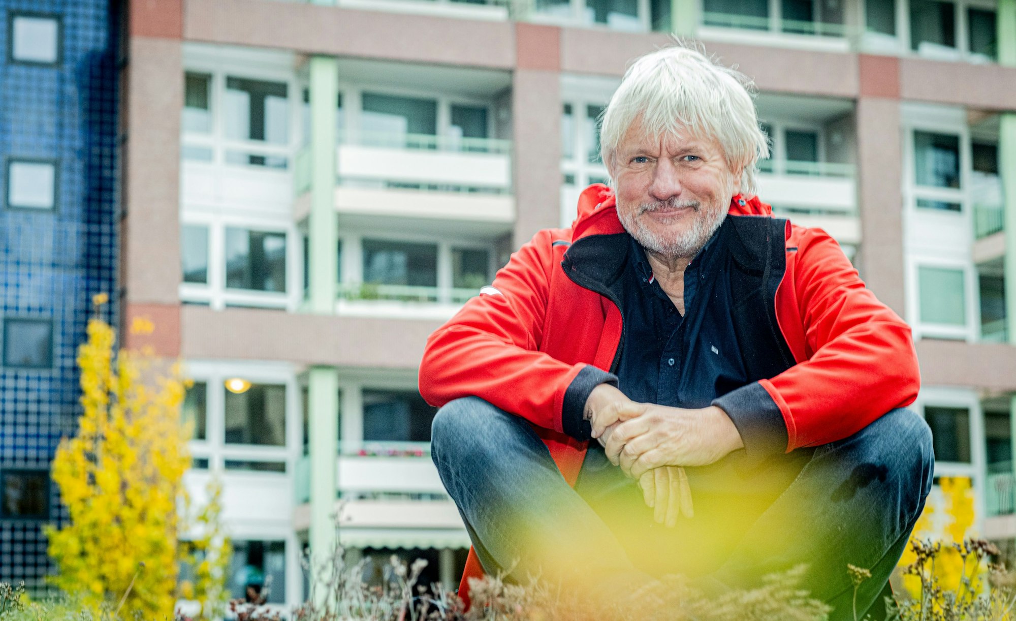Jürgen Becker sitz im Schneidersitz und lächelt.