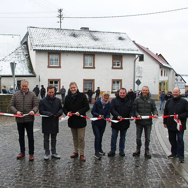 Vertreter aus Kreis, Gemeinde und Versorgern halten ein rot-weißes Flatterband in den Händen, das sie durchschneiden.