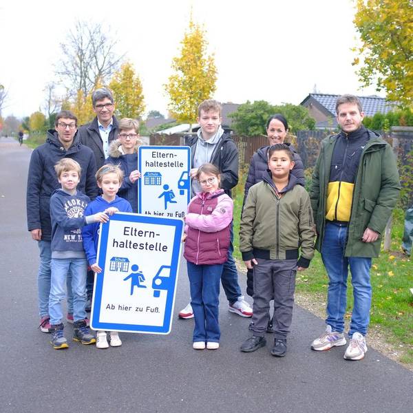 Auf dem Foto Kinder und Jugendliche, Lehrer und Erwachsene zu sehen. Die Kinder halten Schilder mit der Aufschrift „Elternhaltestelle - Ab hier zu Fuß"