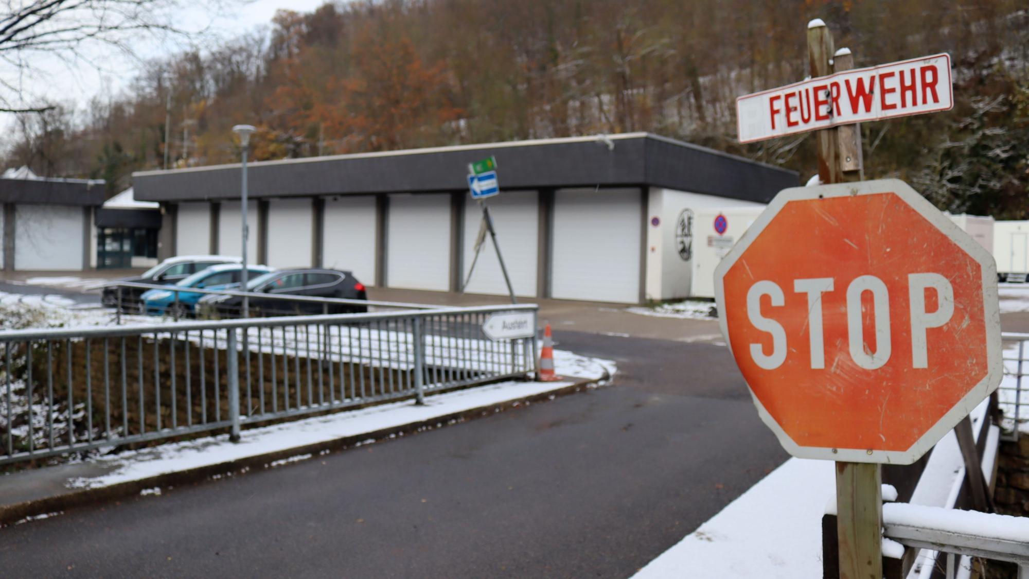 Ein Stoppschild ist an einer Brücke angebracht, darüber hängt ein Schild mit der Aufschrift Feuerwehr. Im Hintergrund ist das Feuerwehrgerätehaus von Bad Münstereifel zu sehen.