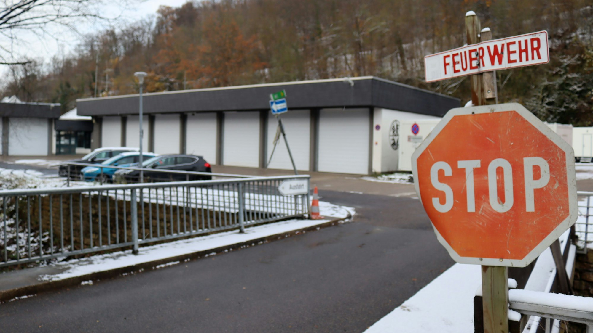 Ein Stoppschild ist an einer Brücke angebracht, darüber hängt ein Schild mit der Aufschrift Feuerwehr. Im Hintergrund ist das Feuerwehrgerätehaus von Bad Münstereifel zu sehen.