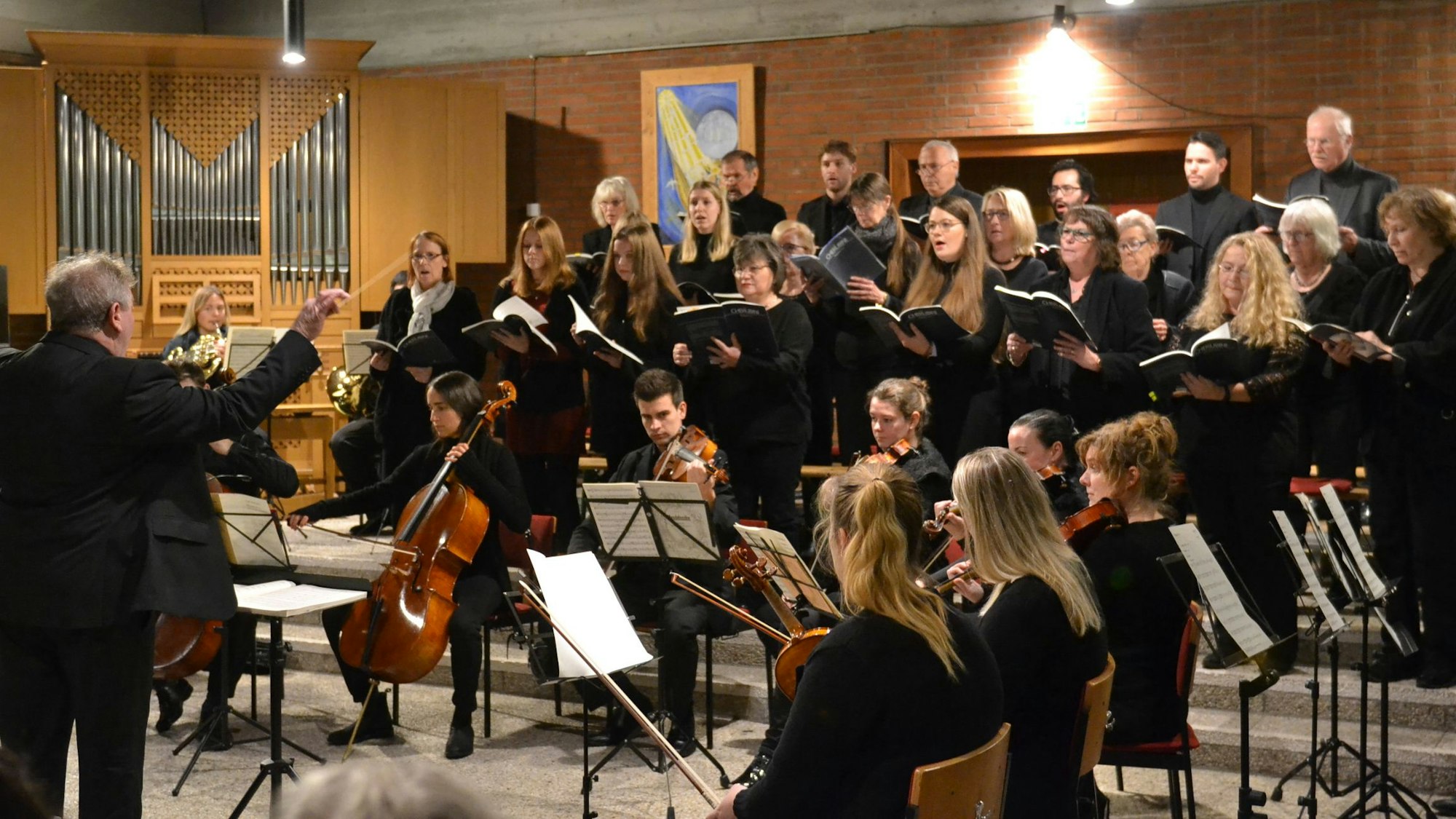 Ein Chor singt in schwarzer Kleidung, davor sitzt ein keines Orchester.