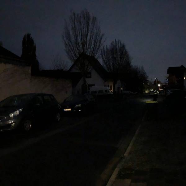 Ein Straßenzug ist nur sehr schwach beleuchtet, es sind nur Umrisse von Häusern, Bäumen und Autos zu sehen.