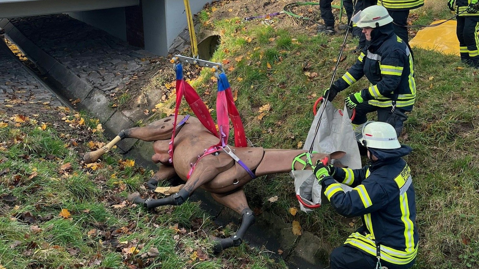 Das Foto zeigt zwei Feuerwehrleute, die das künstliche Pferd aus einem Graben retten.