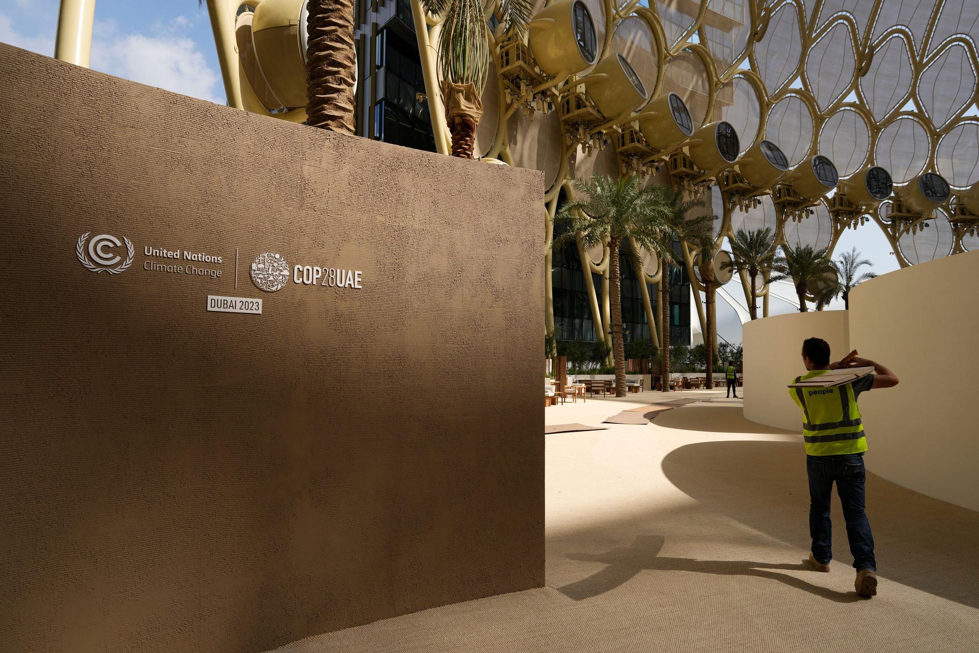 29.11.2023, Vereinigte Arabische Emirate, Dubai: Ein Arbeiter trägt vor dem Beginn des UN-Klimagipfels COP28 ein Schild.