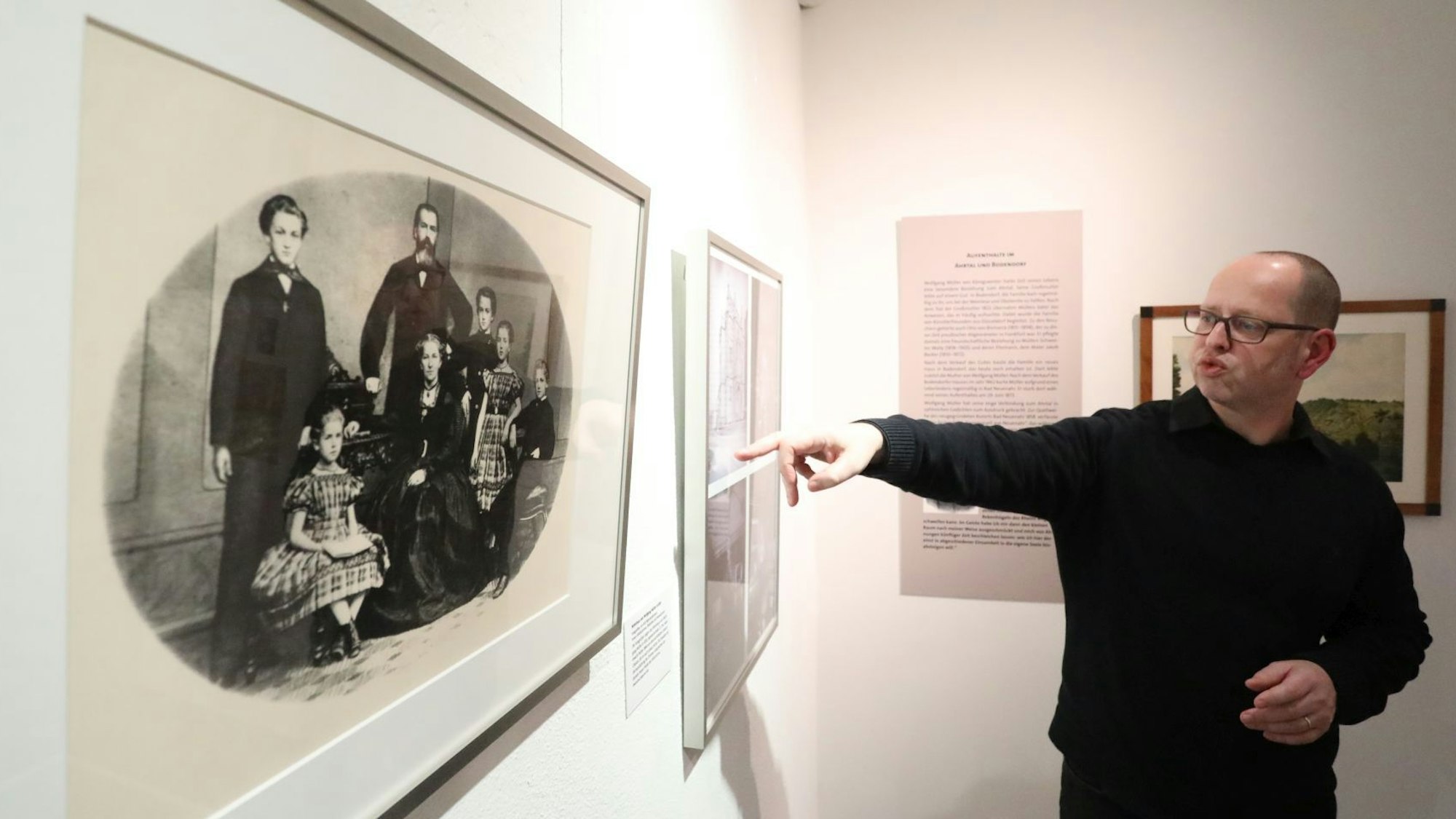 Ein Mann zeigt auf ein historisches Schwarz-Weiß-Foto, das die Familie von „Wolfgang Müller von Königswinter“ zeigt.
