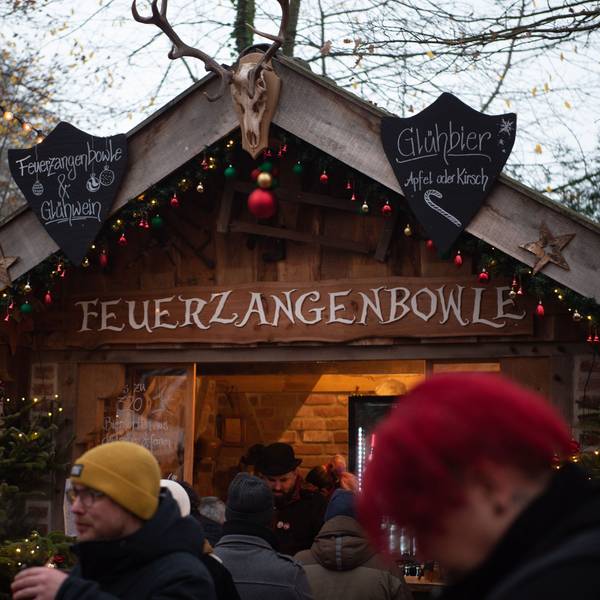 An einer mit roten, grünen und goldenen Weihnachtskugeln geschmückten Holzbude steht „Feuerzangenbowle“.