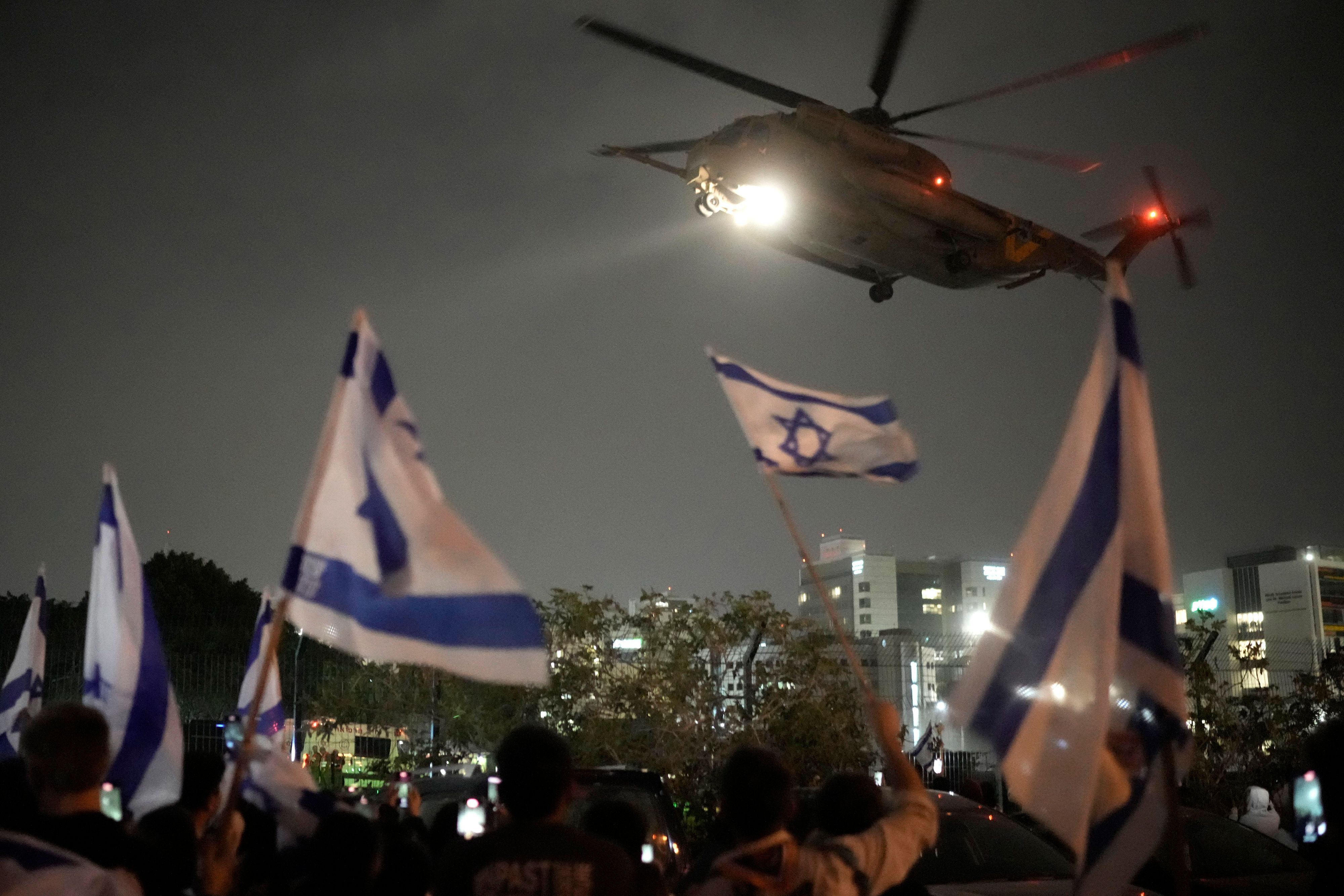 Menschen schwenken israelische Fahnen, während ein Hubschrauber mit Geiseln, die von der Hamas aus dem Gazastreifen frei gelassen wurden, auf dem Hubschrauberlandeplatz des Schneider Children's Medical Center landet.