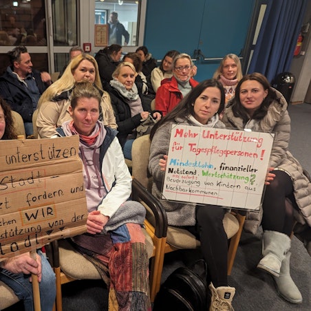 Eine Gruppe von Frauen mit zwei Protestplakaten auf den Zuschauerplätzen im Deutschordensaal des Bürgerhauses.