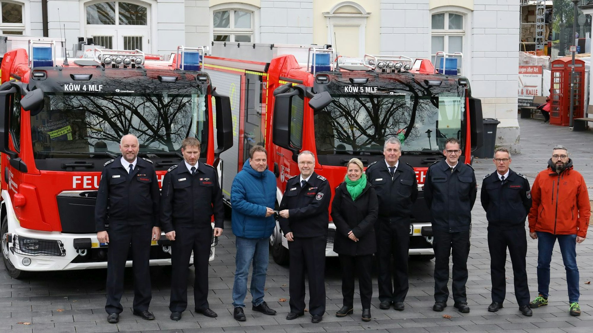 Eine Gruppe von acht Männern und einer Frau steht vor zwei neuen Löschfahrzeugen, die vor dem Rathaus der Stadt Königswinter geparkt sind.