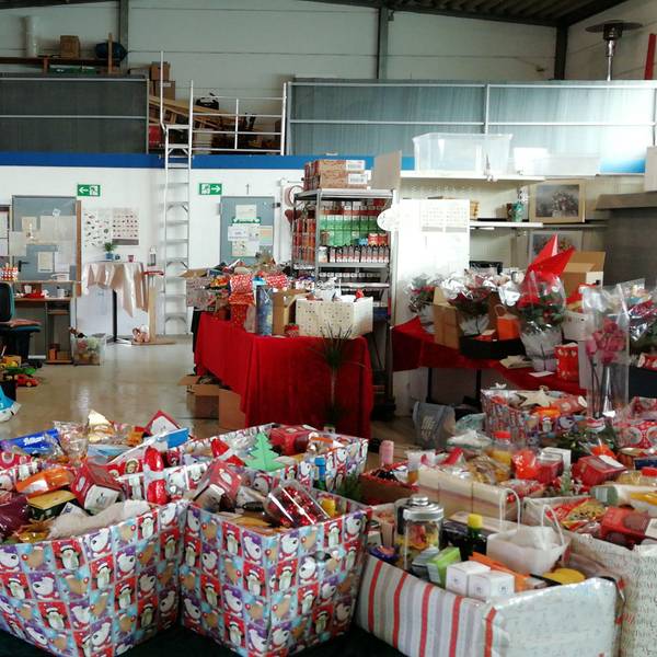 In der Halle der Zülpicher Tafel stehen viele weihnachtlich-dekorierte Kiste mit allerhand Plätzchen, Backzutaten und anderen Leckereien gefüllt.