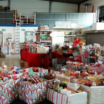 In der Halle der Zülpicher Tafel stehen viele weihnachtlich-dekorierte Kiste mit allerhand Plätzchen, Backzutaten und anderen Leckereien gefüllt.