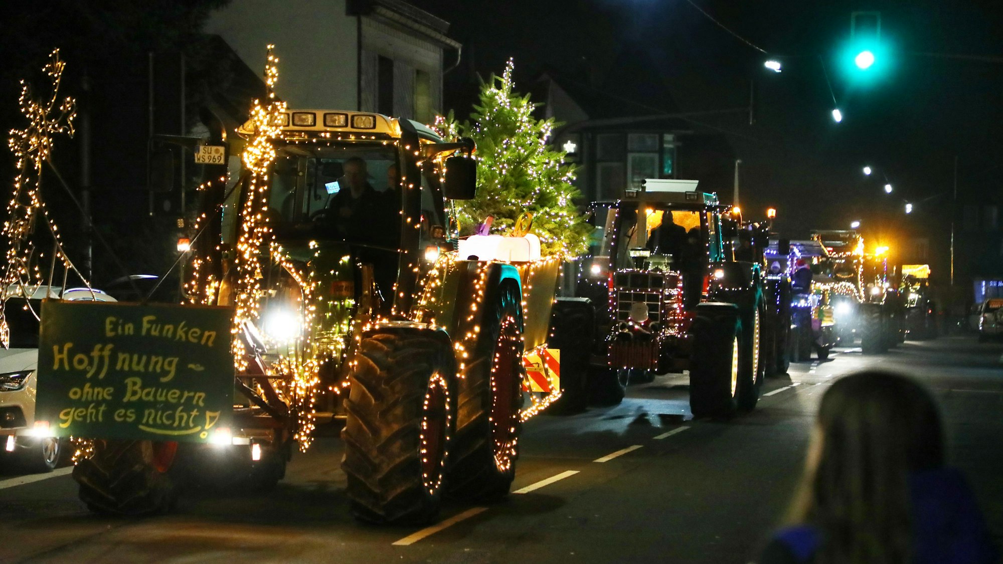 Mit Lichterketten verzierten Traktoren fahren in einer Kolonne über eine Straße.