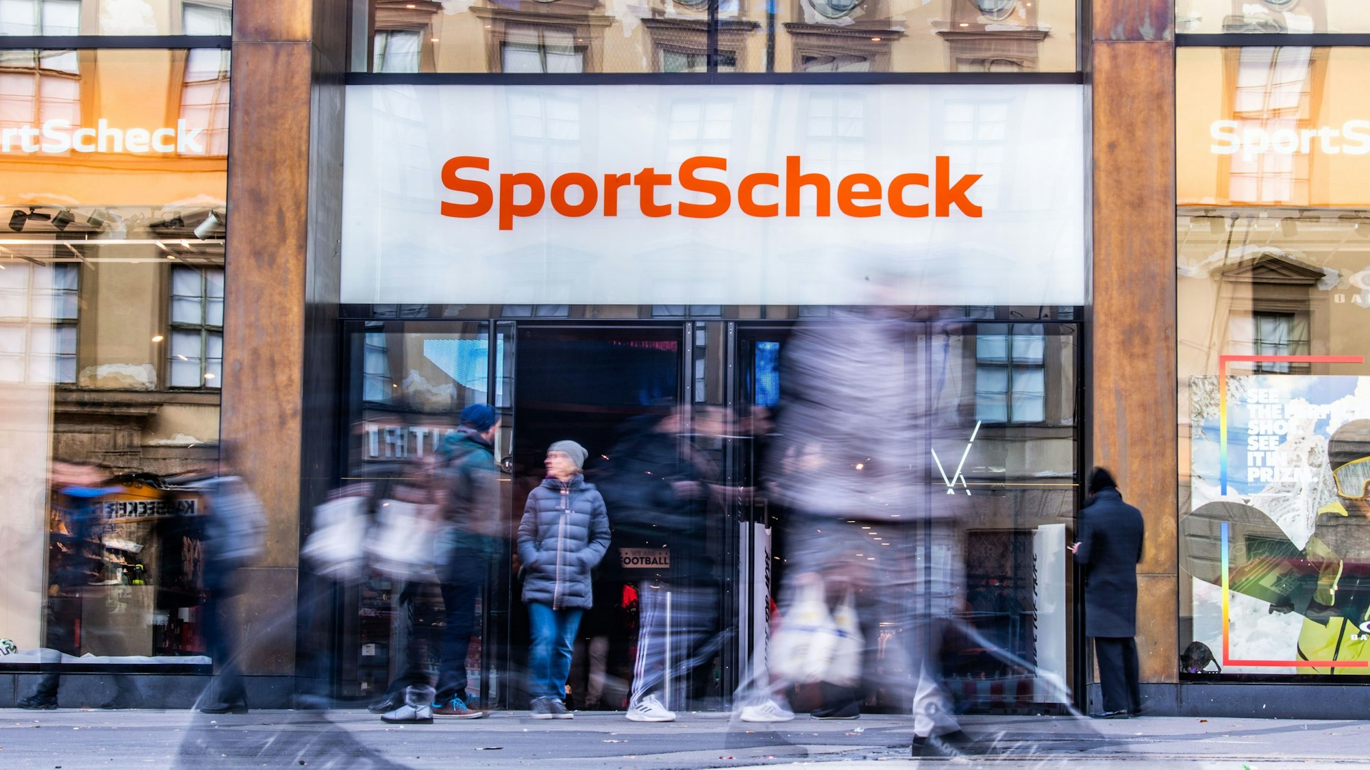 ARCHIV - 11.12.2019, Bayern, München: Personen gehen an einer Sportscheck-Filiale in der Münchener Fußgängerzone vorbei.