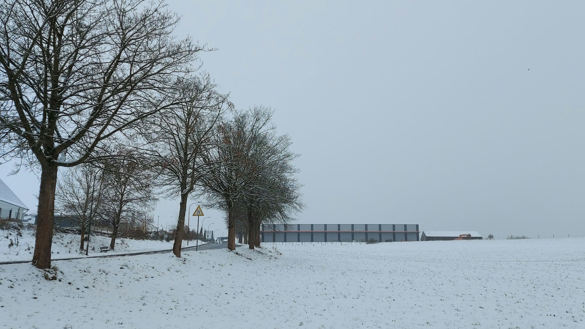 Gezeigt wird ein verschneiter Acker, am linken Bildrand befinden sich Häuser.
