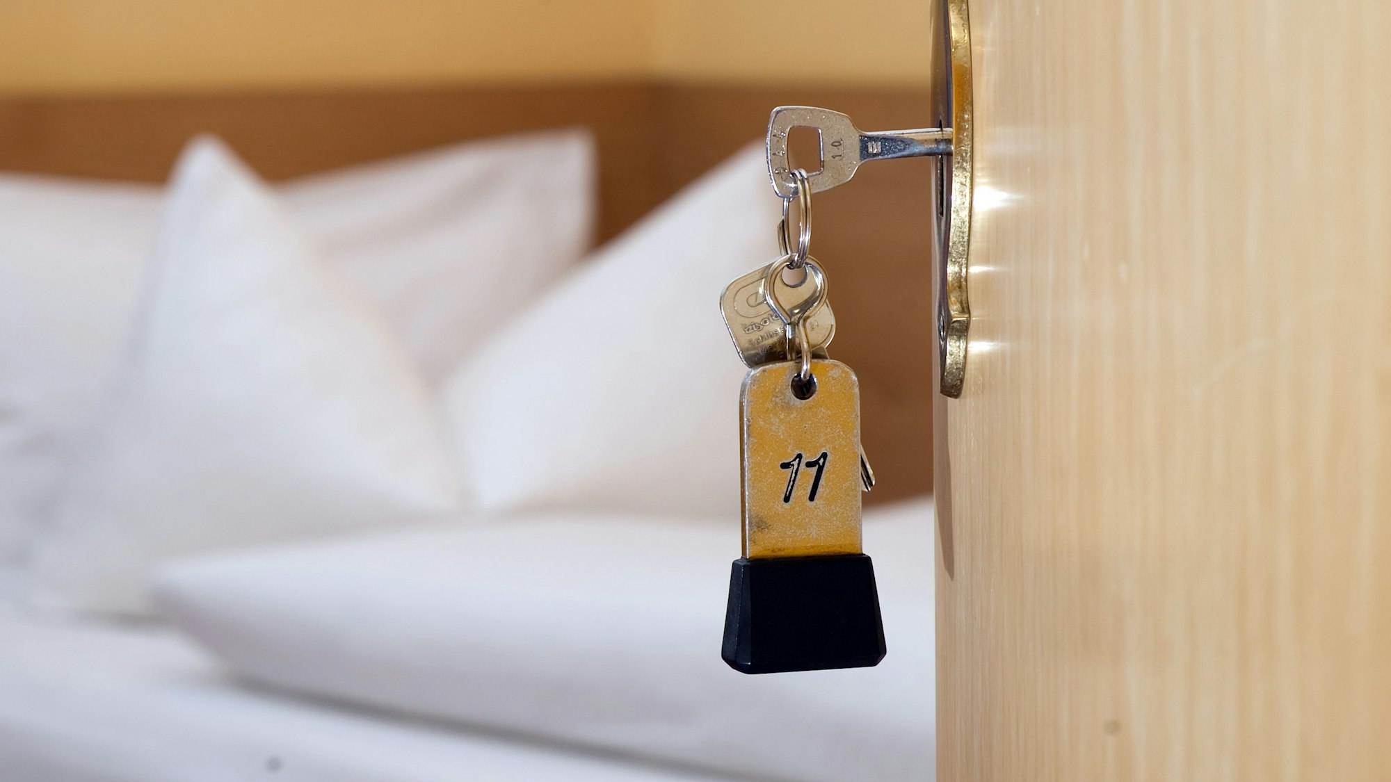 Ein Zimmerschlüssel hängt in einem Hotel vor einem Bett im Türschloss. (Symbolbild).