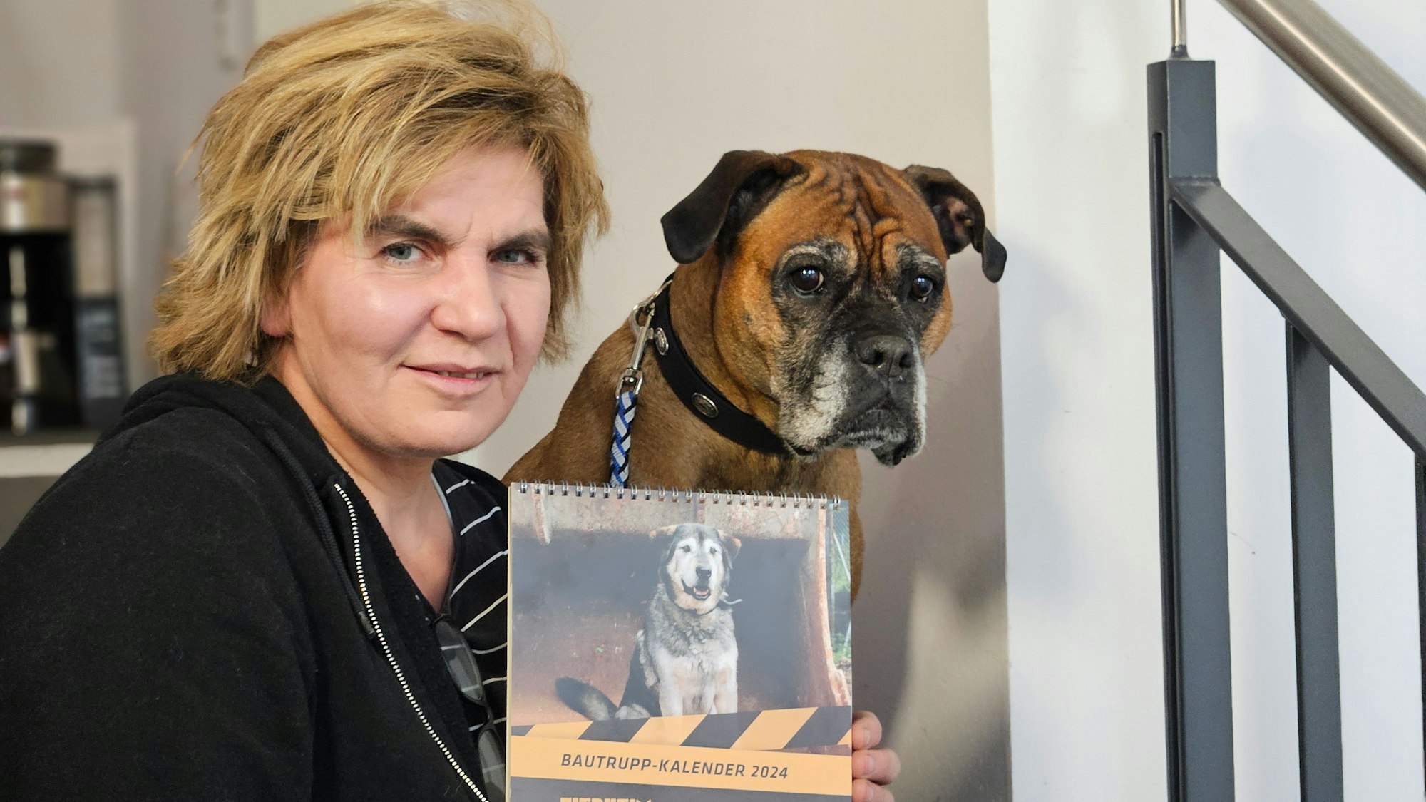 Ein Hund sitzt neben einer Frau, die einen Hundekalender in der Hand hält.