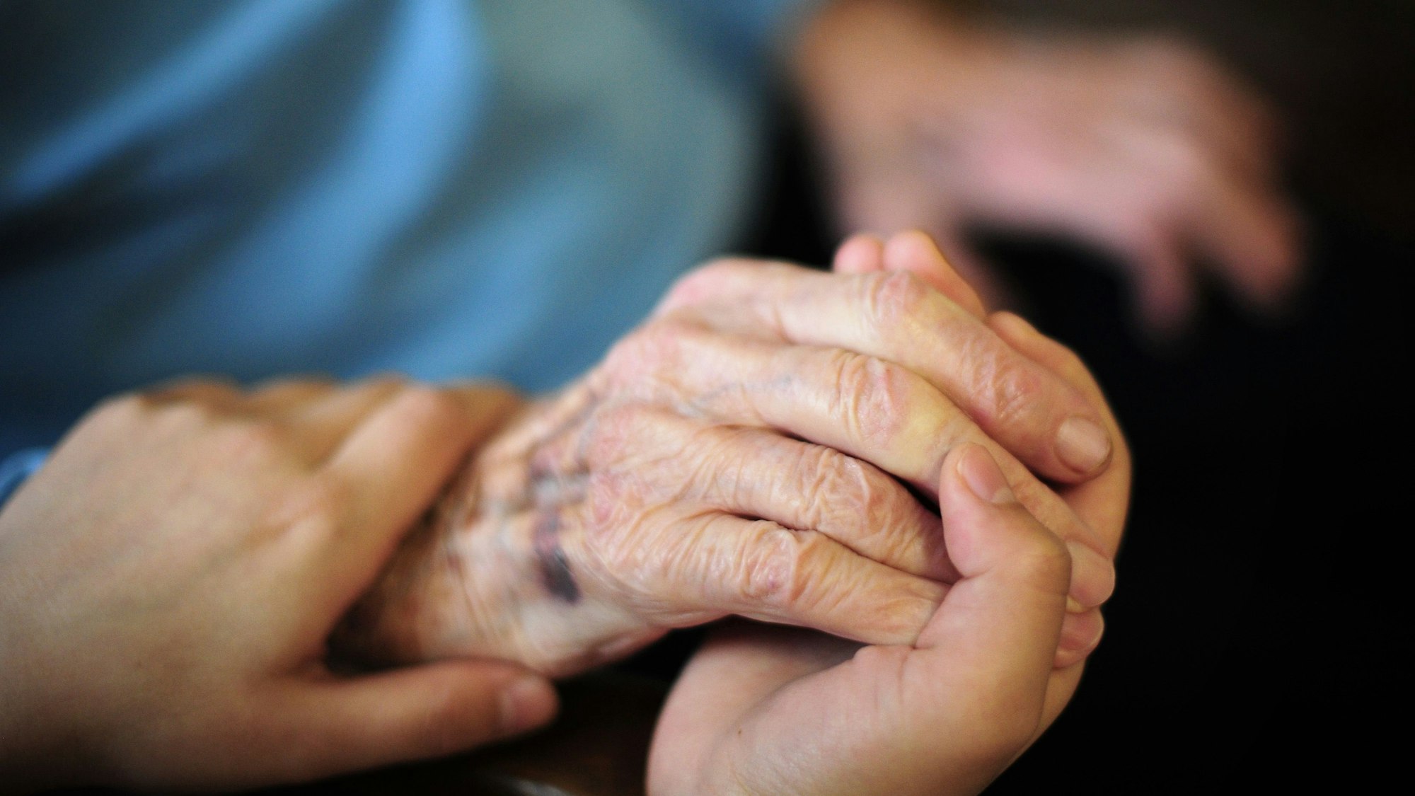 ARCHIV - 23.01.2014, Hessen, Frankfurt/Main: Eine Pflegekraft hält in einem Seniorenheim die Hand einer Bewohnerin.