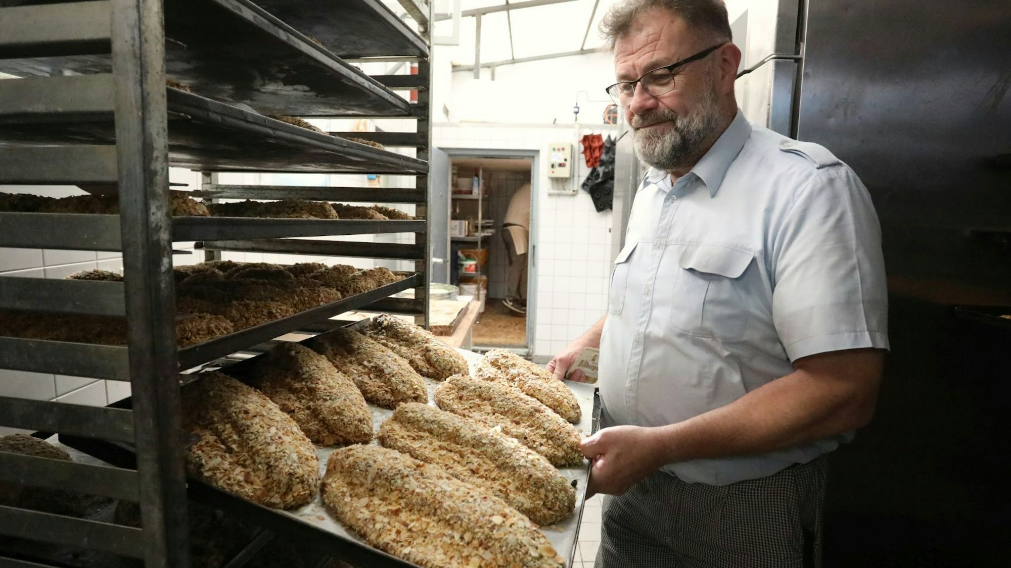 Ein Mann zeigt in der Backstube gerade fertiggestellte Stollen, die auf einem Kuchenblech liegen.