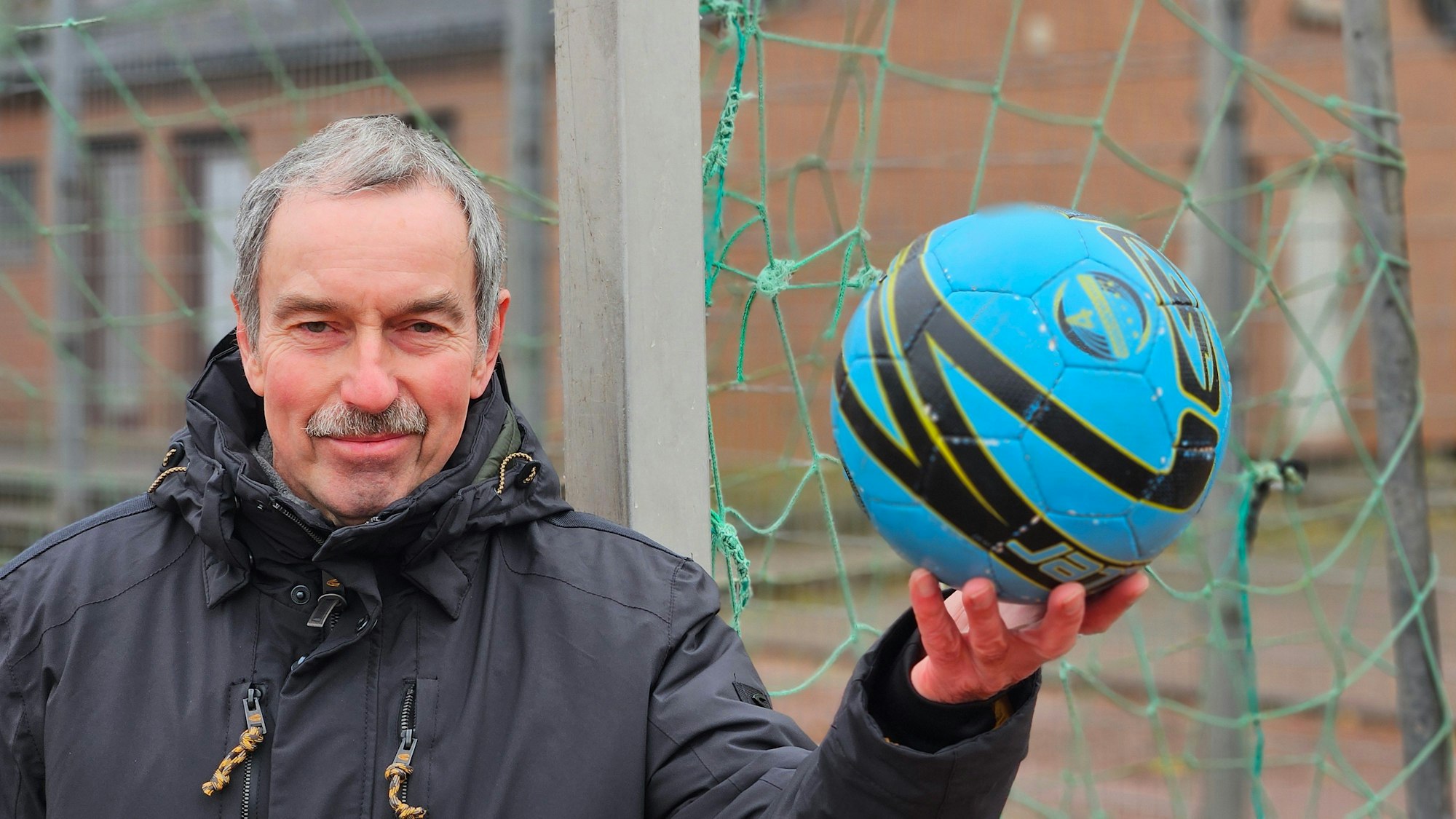 Ein Mann hält einen blauen Fußball in der Hand.