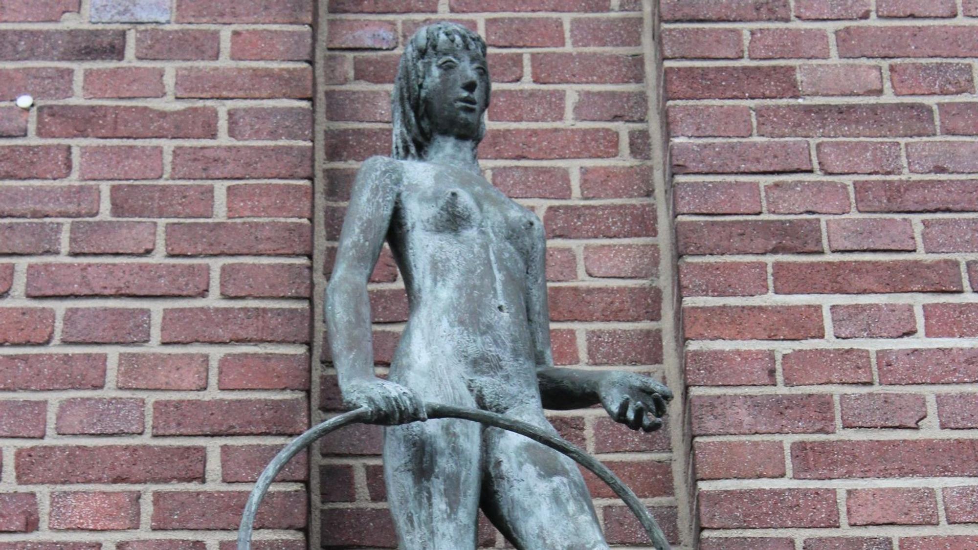 Das Bild zeigt die Skulptur eines Mädchens, das einen Reifen in der Hand hält.