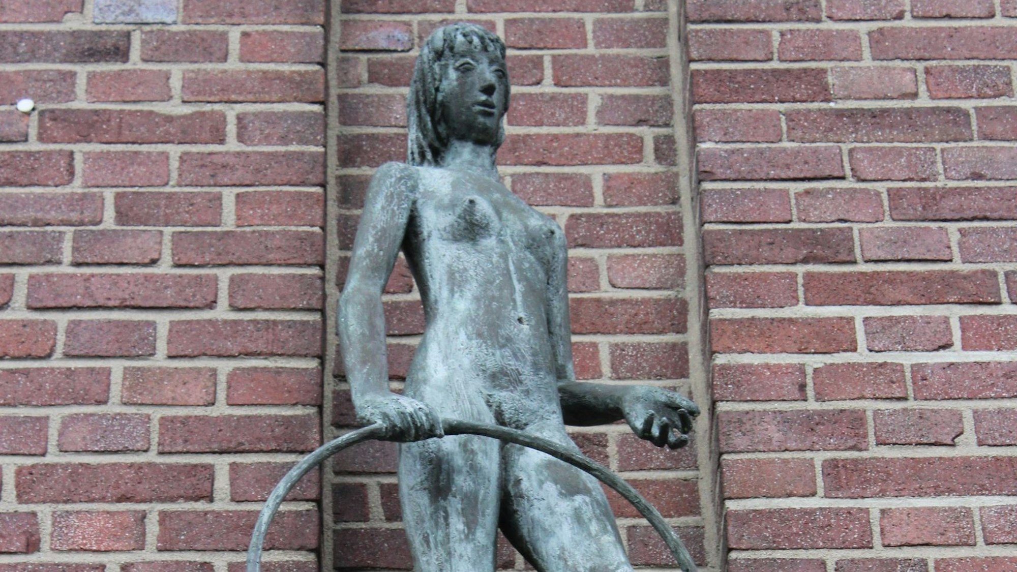 Das Bild zeigt die Skulptur eines Mädchens, das einen Reifen in der Hand hält.