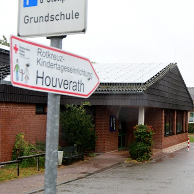 Auf einem Wegweiser steht "Rotkreuz-Kindertageseinrichtung Houverath", dahinter ist der Kindergarten zu sehen.