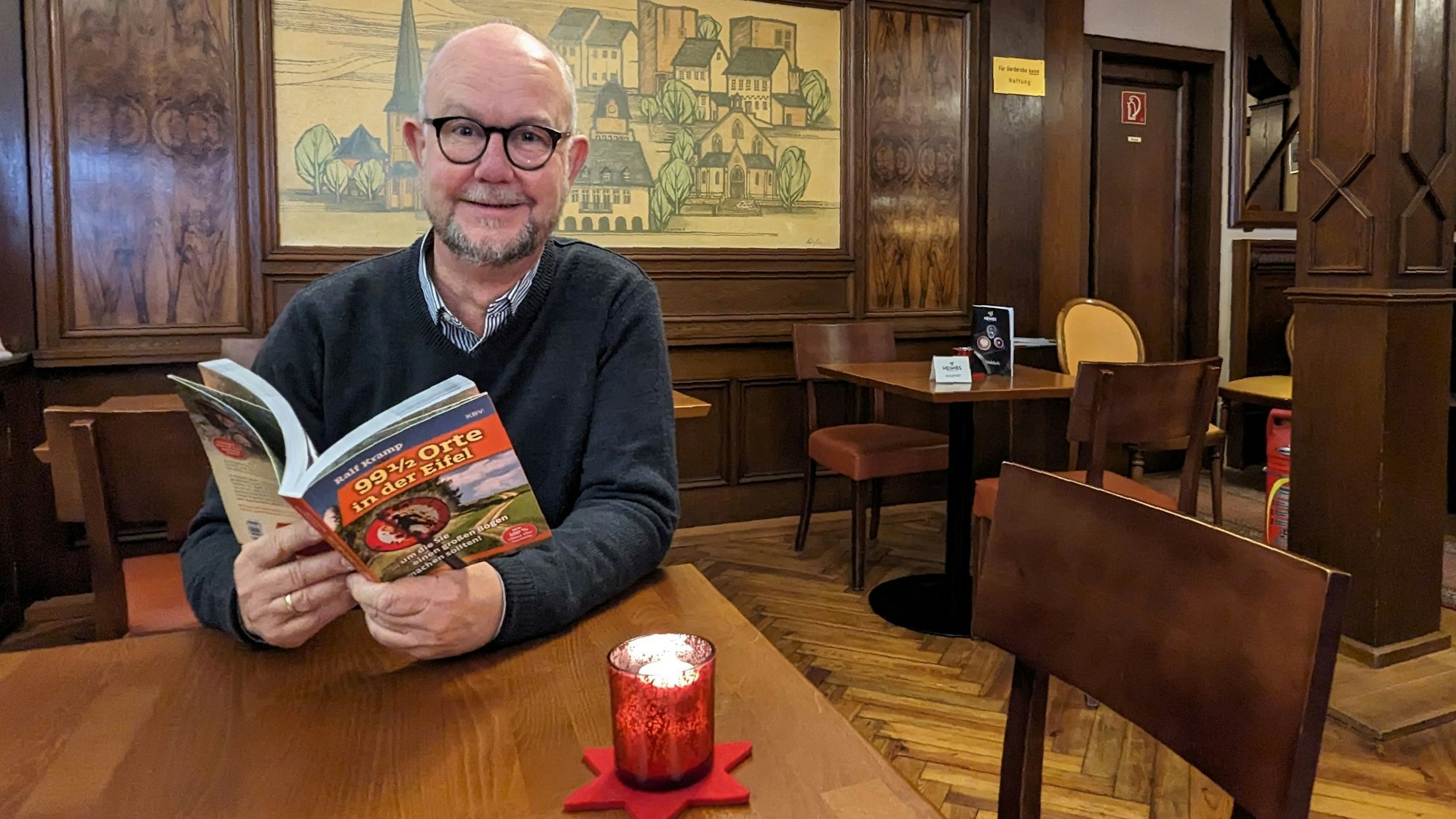 Autor und Verleger Ralf Kramp sitzt mit einem aufgeschlagenen Buch im Café Kramer in Euskirchen.