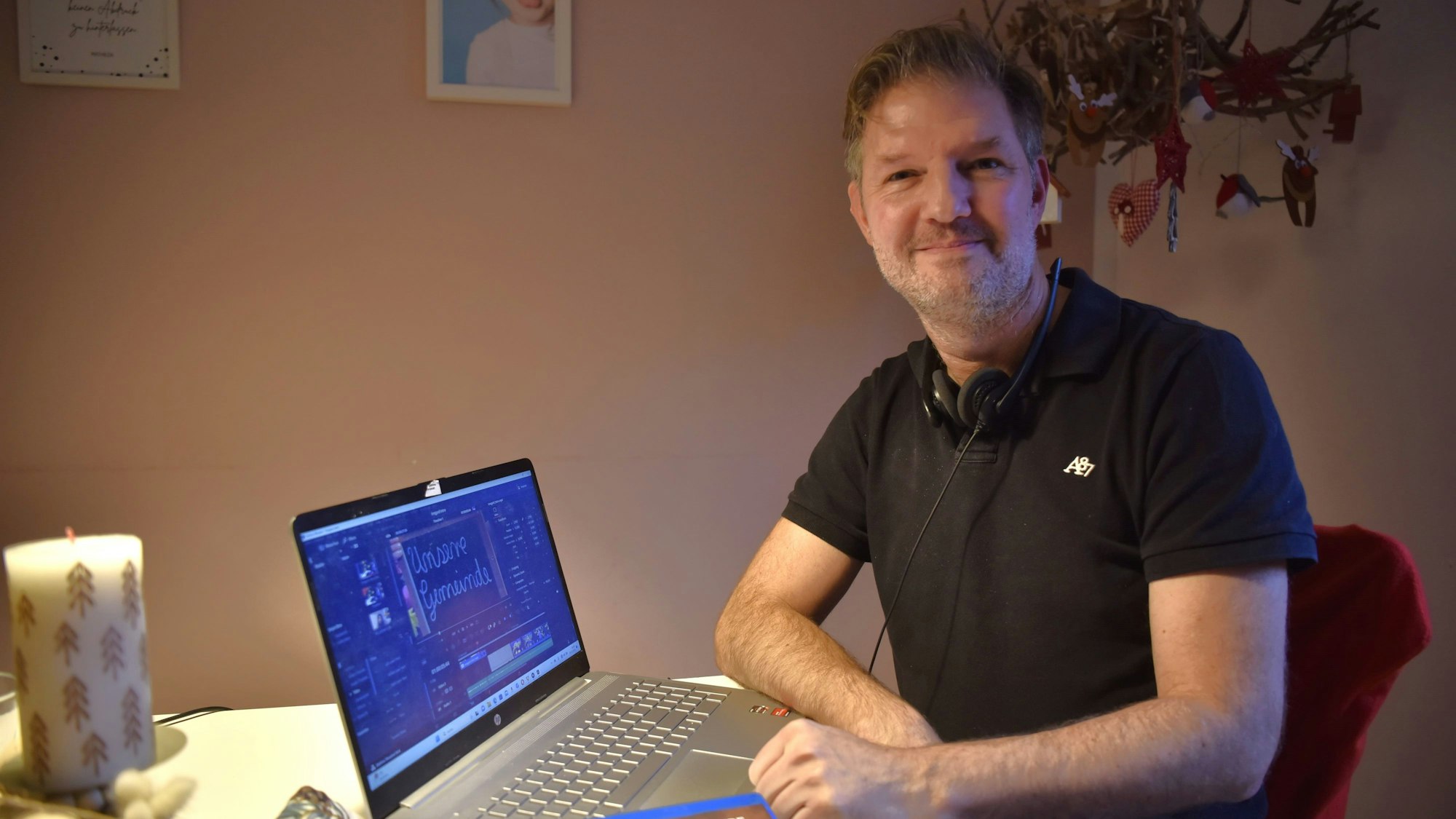 Stephan Gatzweiler sitzt an einem adventlich dekorierten Tisch, vor ihm steht ein Laptop, auf dem ein offenes Schnittprogramm zu sehen ist.