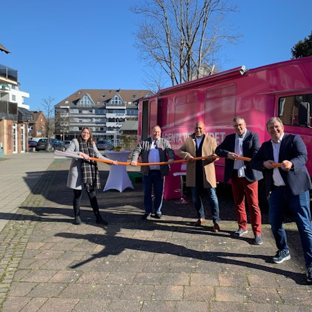 Vertreter der Stadt Niederkassel und der Telekom halten ein dickes Glasfaserkabel in der Hand. Im Hintergrund steht ein magentafarbenes Infomobil der Telekom.