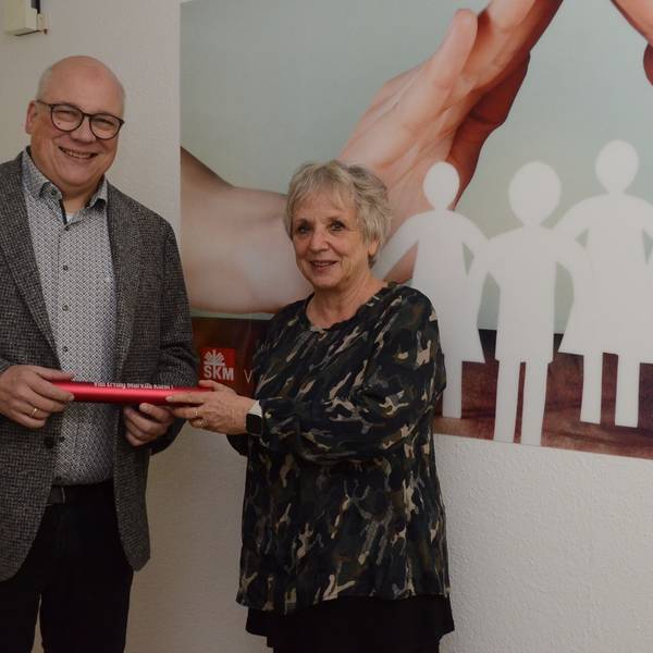 Ein Mann mit Glatze und Brille nimmt einen roten Staffelstab aus Metall in Empfang. Eine Frau mit grauen Haaren überreicht das Rohr.