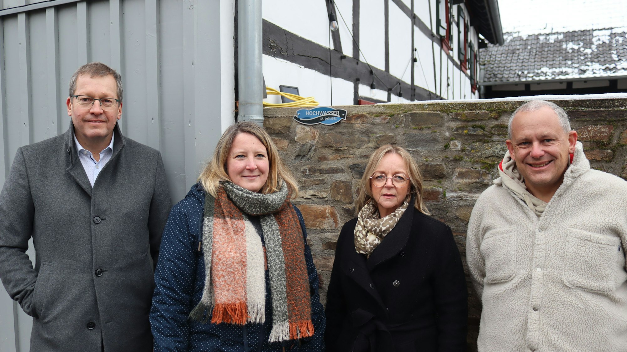Peter Schellenberger, Stefanie Liebing, Sabine Preiser-Marian und Peter Greven stehen vor einem Haus. Im Hintergrund sieht man die Flutmarke an einer Mauer.